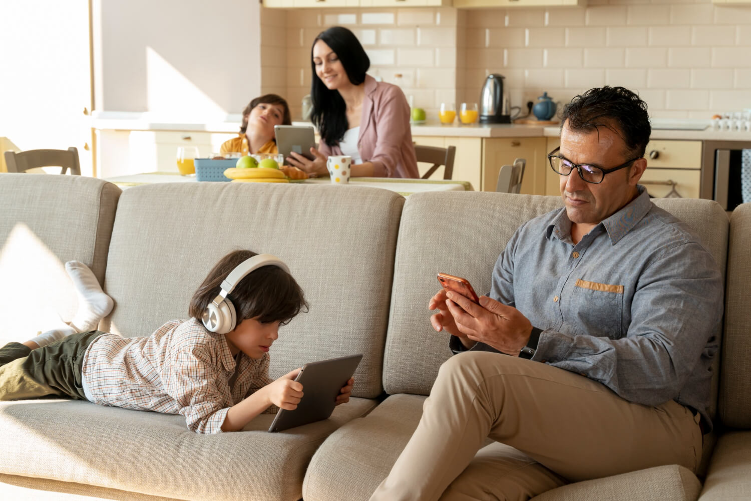 A father and son sitting on a couch together, while and mother and son sit together at a table in the foreground.